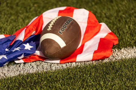 American football on green grass, on flag of United States of America background.