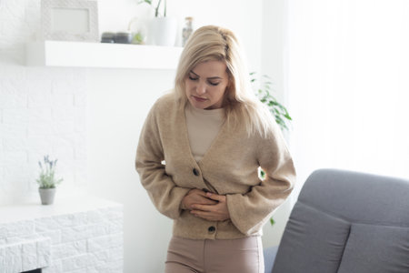 Woman having stomach ache, bending and holding hands on belly, discomfort from menstrual cramps.の写真素材