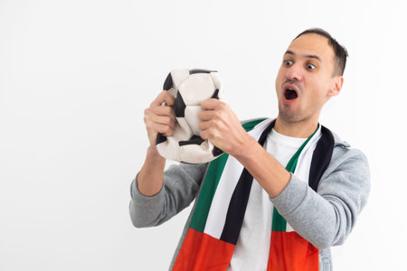 Handsome american man playing footbal holding soccer ball over white background shouting and...