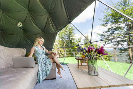 middle aged woman uses a laptop resting and spending time at Glamping house on holidays. holiday dome tent. Cozy, camping, hygge, lifestyle conceptの写真素材