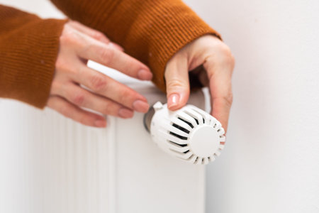 Woman warming hands on heating radiator near white wall, closeupの写真素材