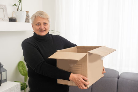 Elderly woman unpacking things in new house. Female hands opening cardboard box. Real estate, purchase, moving concept.の写真素材