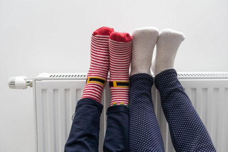 Mother and child warming feet near heater at home, closeup