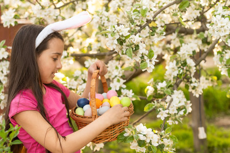 A little girl with pink rabbit ears. painted eggs in the park. Easter. Copy space.