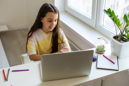 Photo of positive kid girl study remote sit desk table use laptop have online communication lesson...