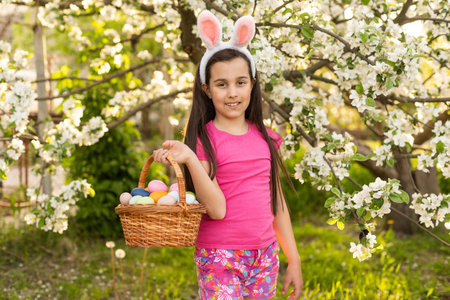 A little girl with pink rabbit ears. painted eggs in the park. Easter. Copy space.