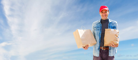 Young Delivery Man Carrying Cardboard Box In Front Of sky background