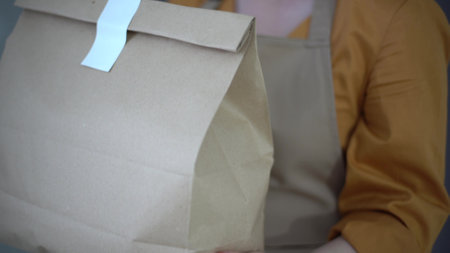 Woman giving fast food order isolated on white background. Female courier holding paper packet with food, coffee. Products delivery from shop or restaurant to home. Copy spaceの写真素材