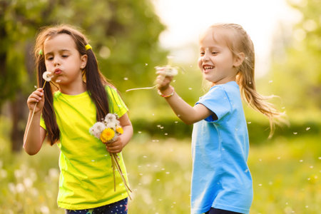 two little girls with dandelions little sister on the background of spring meadow.の写真素材