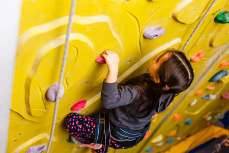little girl climbing a rock wall indoor.