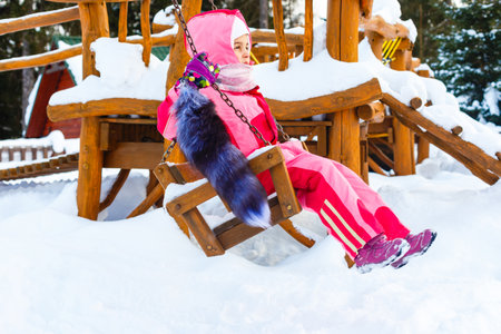 Charming little girl on swing in snowy winterの写真素材