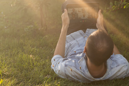 Young man in the garden in summer on the laptop computer while chatting online as a freelancer.