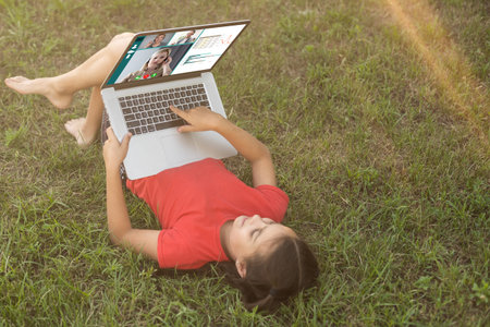 little girl learns, a teenager working on laptop lying on a meadow. mobile Internet in rural areas....