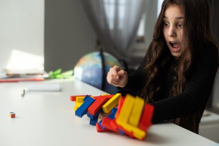 a little happy girl is playing the board game wooden block at the table. Construction of a tower...