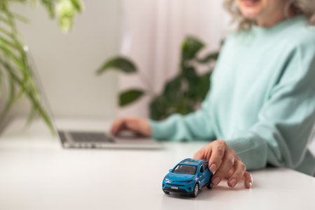 hands of a woman on a desk behind a keyboard with a small model car. Insurance concept.の写真素材