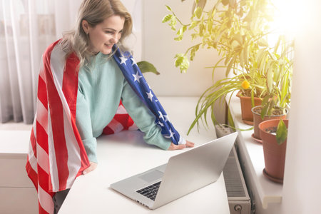 Positive teacher in headset having online lesson on laptop near flags in schoolの写真素材