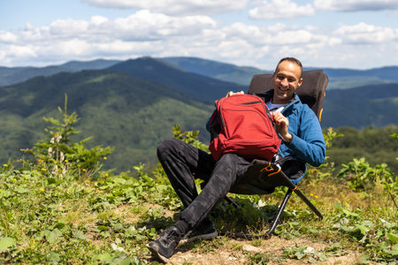 idyllic and rural scene. A man chilling and resting after hiking sitting on a chair and looking in the mountainsの写真素材