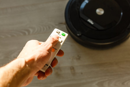 Close-up Of A Man Holding Remote Control Of Robotic Vacuum Cleaner To Start Cleaning.
