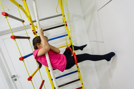 Children Activity Concepts. Little Caucasian Girl Having Stretching Exercises on Wall Bars Indoors.