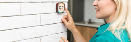 woman regulating heating temperature with a modern wireless thermostat installed on the white wall...