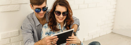 Happy couple with tablet, shopping online, making internet order sitting at home floor in empty living roomの写真素材