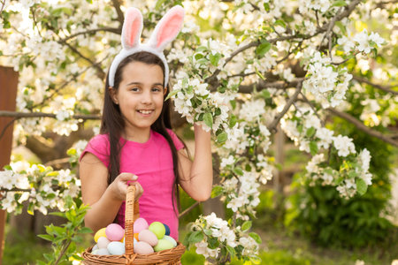 A little girl with pink rabbit ears. painted eggs in the park. Easter. Copy space.