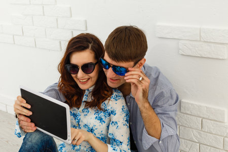 Simple happiness. Cheerful lovely couple cuddling on sofa at home, using digital tablet for websurfing, free spaceの写真素材