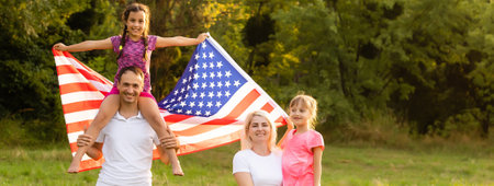 Happy family sitting together in their backyard holding the american flag behind them. Smiling couple with their kids celebrating american independence day holding american flagの写真素材
