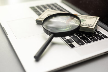 Magnifying glass and dollar bills on laptop. Search for financial income on Internet.の写真素材