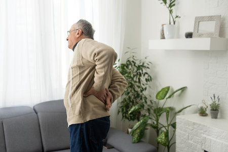 Caucasian old senior elderly unhealthy sickness grey male grandpa near sofa at home alone holding hands on back having emergency painful muscle and backache injury problem.の写真素材