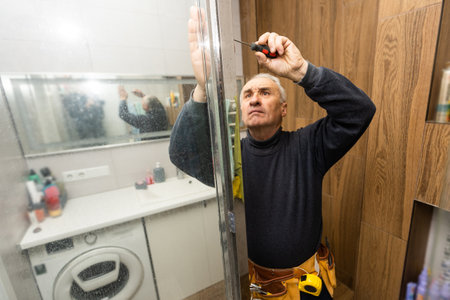 man repairs the shower door in the bathroom. A male repairman repairs the shower cabin.の写真素材