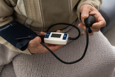 Senior man using a home blood pressure machine to check his vital statistics sitting at the living...