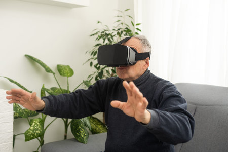 handsome senior man using VR 360 glasses at home. Making browse and tap gestures. Concept of active...