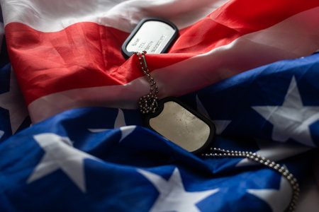 Closeup of a dog tag with the text thank you veterans engraved in it, next to a flag of the United States background.の写真素材