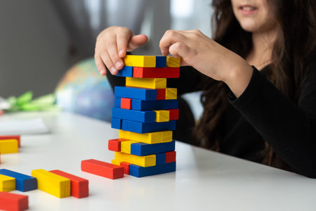 a little happy girl is playing the board game at the table. Construction of a tower made of wooden cubesの写真素材