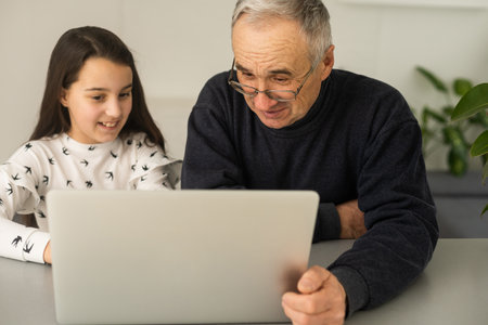 Portrait of senior man and young girl granddaughter using laptop at home.の写真素材