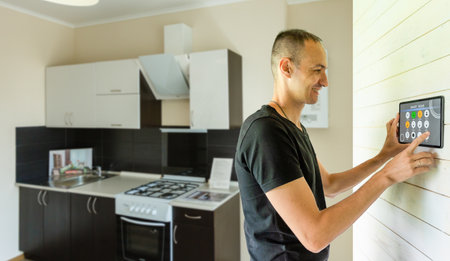 Smart home control application. Man controls household appliances through a smartphone. Hands with a smartphone inside house. Concept - smart home application development. Apps for IOT houseの写真素材