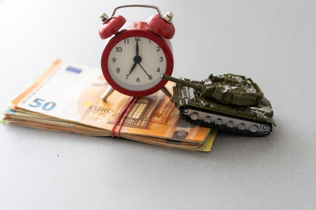 plastic model toy tanks on a pile of euro banknotes against wooden background