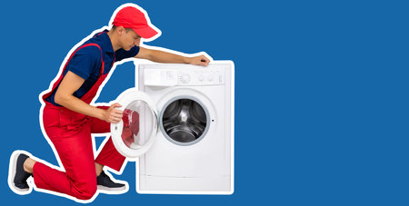 The repairman in worker suit with the professional tools box is fixing the washing machine on a blue backgroundの写真素材