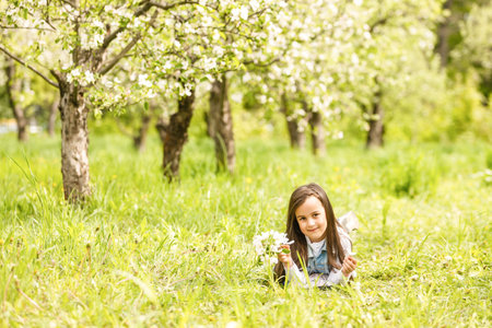 Portrait of cute and pretty little girl in spring blooming trees. Adorable little girl smiling in blooming garden on sunny day. Child and flowers. Childhood & natural tenderness. Childrens day.の写真素材