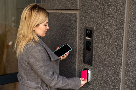 Close up of woman using card intercom at building entrance.