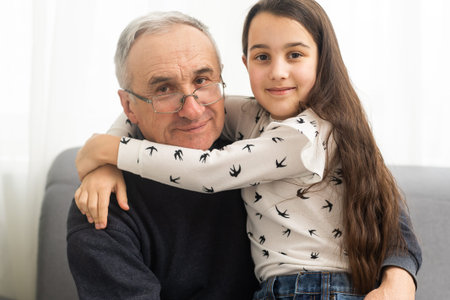Smiling granddad hugging girl while sitting on sofa
