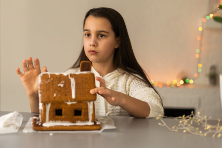 Kids baking Christmas gingerbread house. Children celebrating winter holiday at home. Decorated living room with fireplace and tree. Family activity. Little girl making cookiesの写真素材