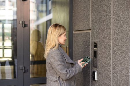 woman standing near the door and locking it with online application on her smartphone
