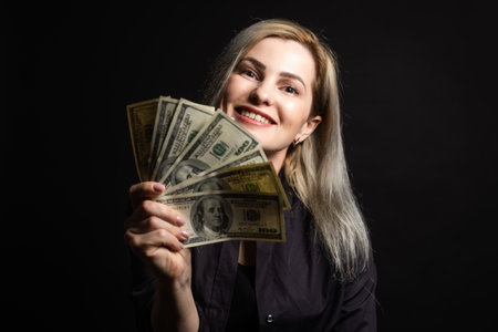 Young fun happy successful employee business woman 30s she wear casual brown classic jacket holding fan of cash money in dollar banknotes isolated on background studio portraitの写真素材
