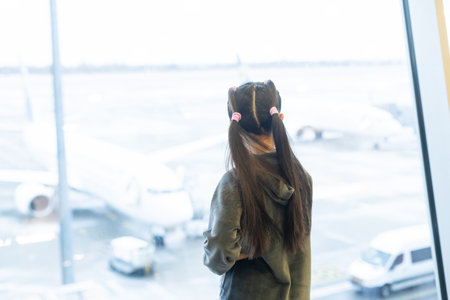 little baby girl waiting boarding to her flight in airport transit hall and looking at airplane parking near departure gate. Travelling by air with childの写真素材