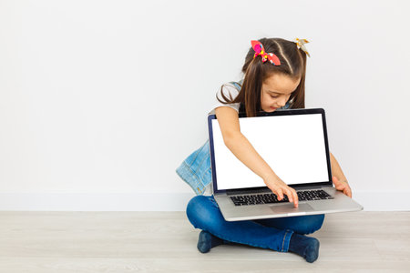 Cute little girl is sitting on floor with her laptop, wearing glasses, isolated over whiteの写真素材