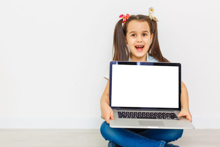 Cute little girl is sitting on floor with her laptop, wearing glasses, isolated over white