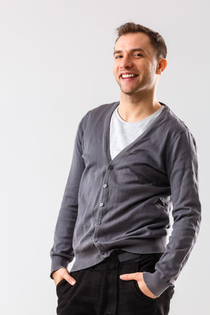 Casually handsome. Confident young handsome man keeping arms crossed and smiling while standing against white backgroundの写真素材