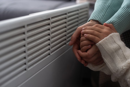 Mother and child warming hands near electric heater at home, closeup.の写真素材